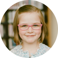 little girl with short blonde hair smiling with pink glasses frame