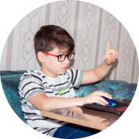 boy inside house learning on a laptop wearing black glasses with red side frame