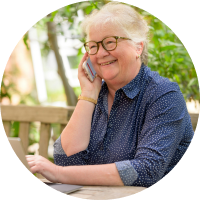 elder woman with white hair and dark glasses frame outside on wooden porch talking on cell phone smiling